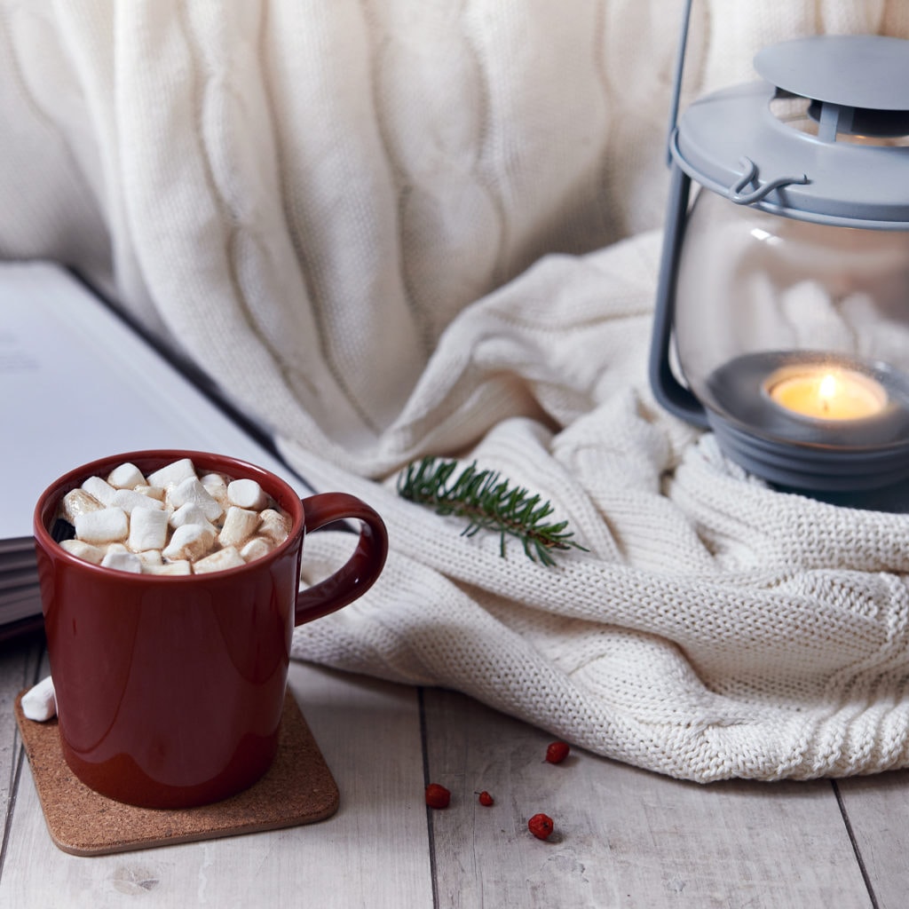 Mug with hot chocolate and marshmellow, white knit cover, book and lantern.