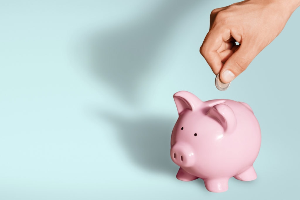 Hand putting coin to piggy bank on blue background.