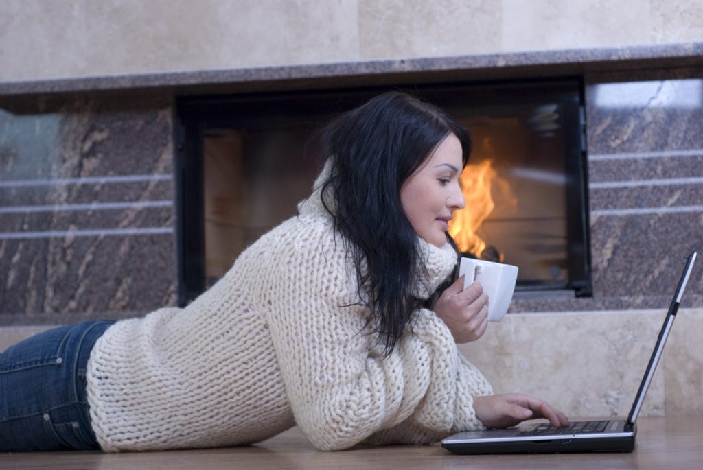 Attractive woman relaxing with a lap top in front of a fireplace.