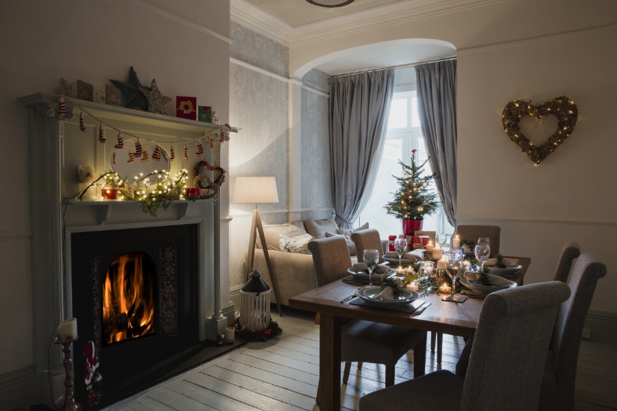 Dining room of a home decorated for Christmas. The table is set ready for Christmas dinner and the fire and candles are lit.