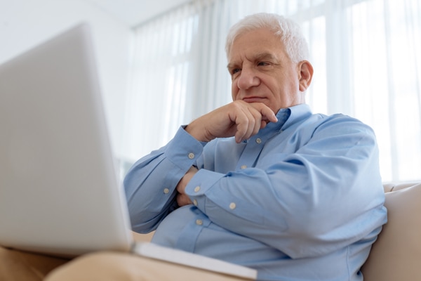 Elderly man sitting on comfy sofa and watching something on laptop