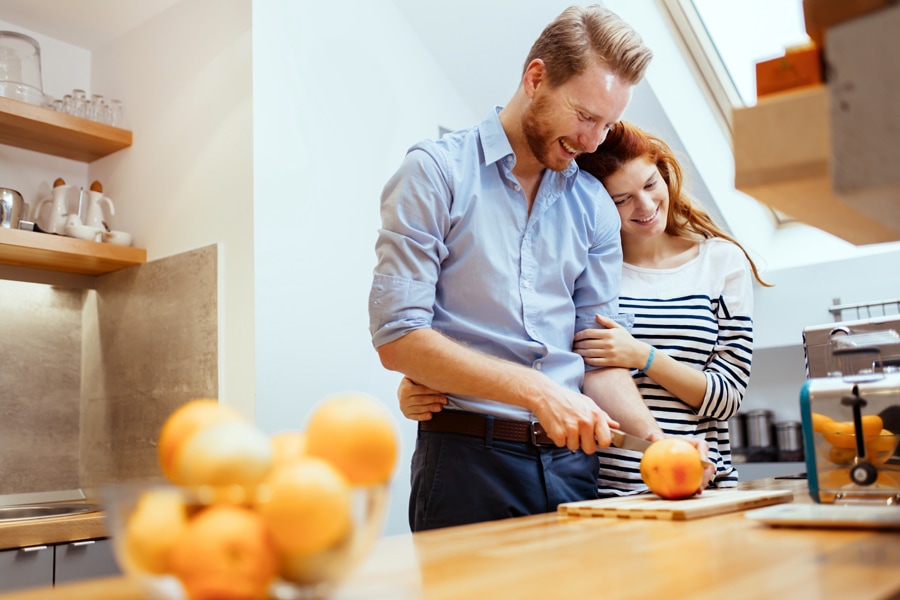 happy couple cutting oranges on a wooden cutting board during the bright, sunny day.