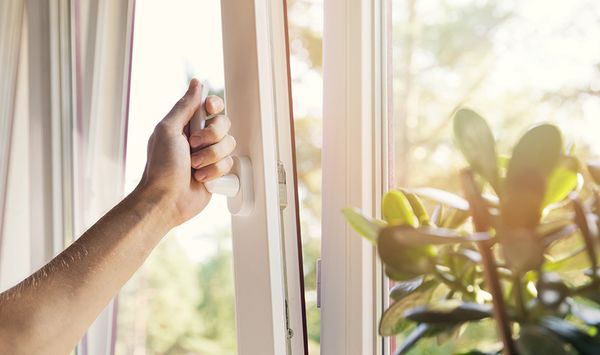 Close up of a hand opening a window on a sunny day to promote indoor air quality.