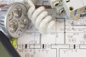 Different types of light bulbs and electrical accessories laying on a house plan print.