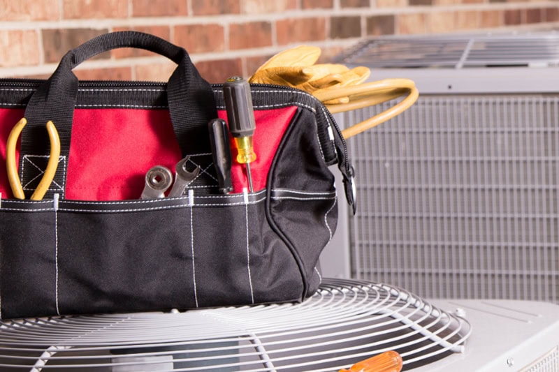 HVAC technician's tool bag sitting on an AC unit outside a home.