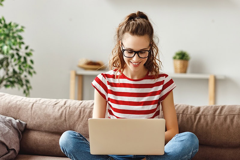 Young woman sitting on her couch searching on her laptop.